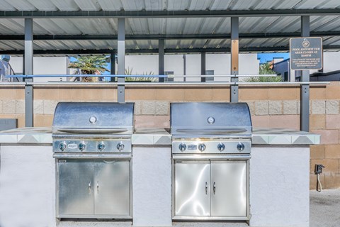 Two stainless steel BBQ grills are on a patio.