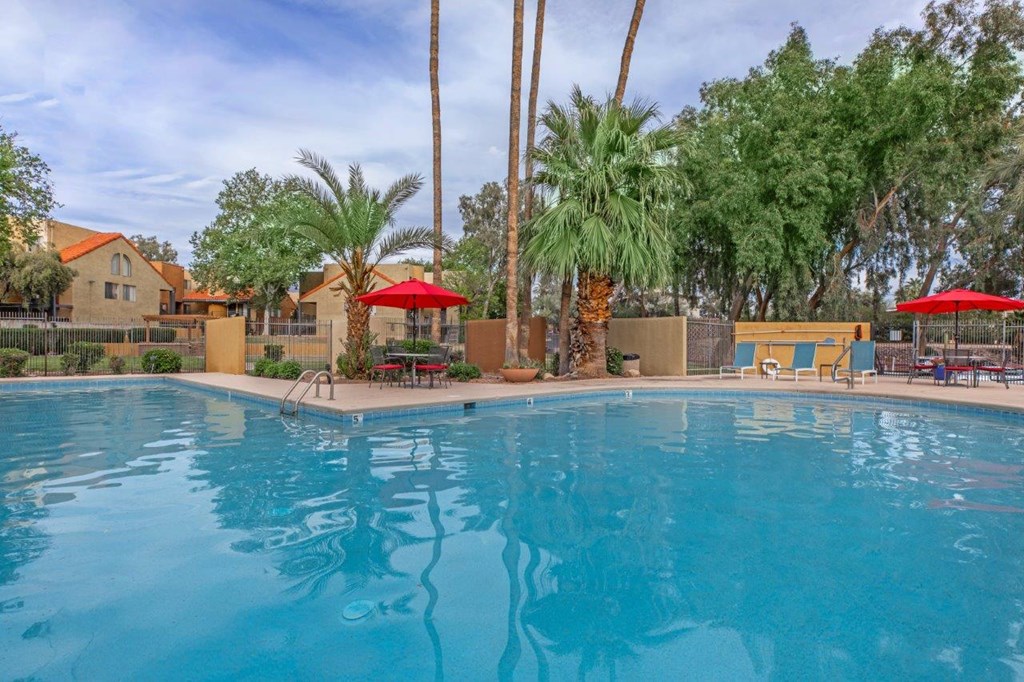 A swimming pool surrounded by palm trees and red umbrellas.