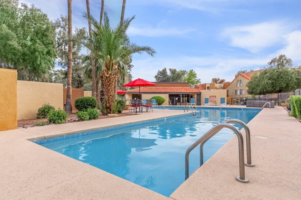 A pool surrounded by palm trees and a red roofed building.