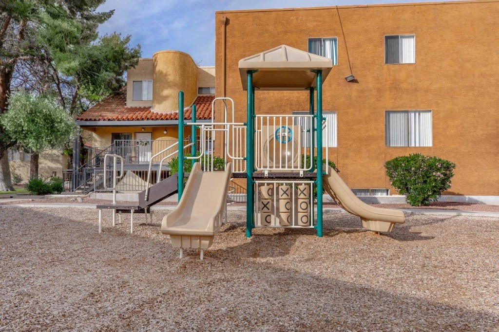 A playground with a slide and a swing set in front of a building.