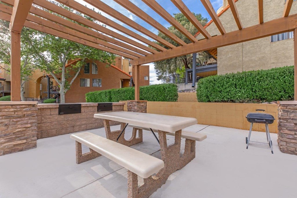 A patio with a picnic table and bench under a wooden pergola.