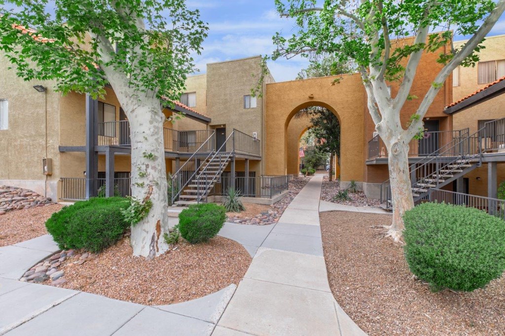 A courtyard with a pathway, trees, and bushes in front of apartment buildings.