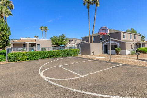 A basketball court is located in front of a building with a basketball hoop.