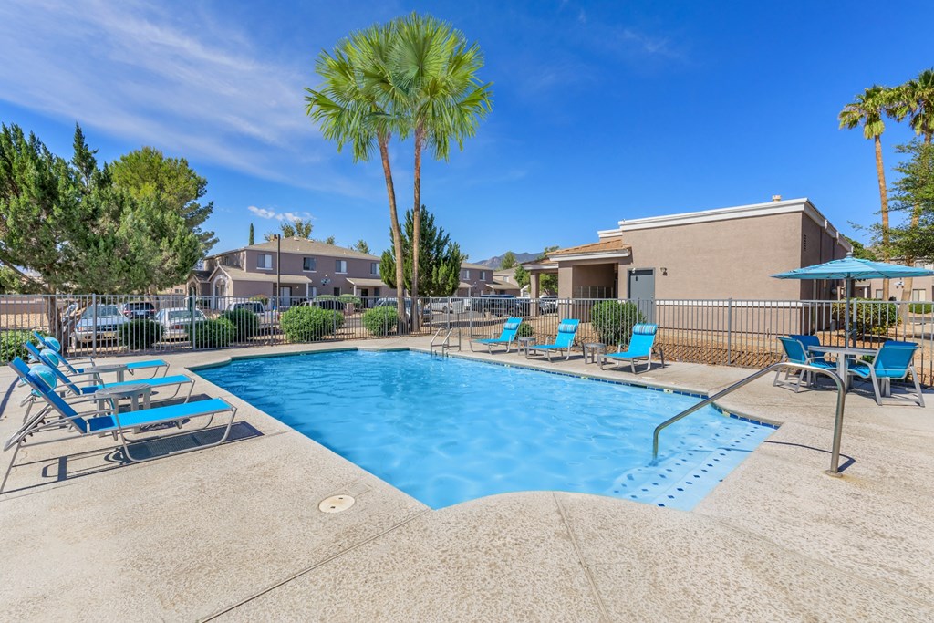 A pool surrounded by chairs and trees with a building in the background.