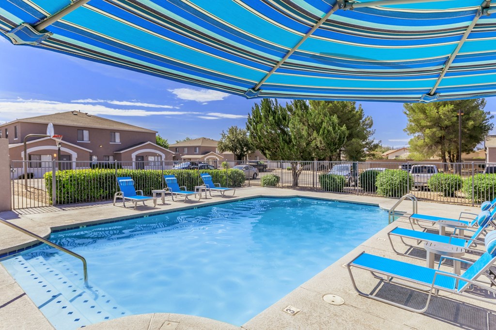 A pool with a blue canopy and lounge chairs.