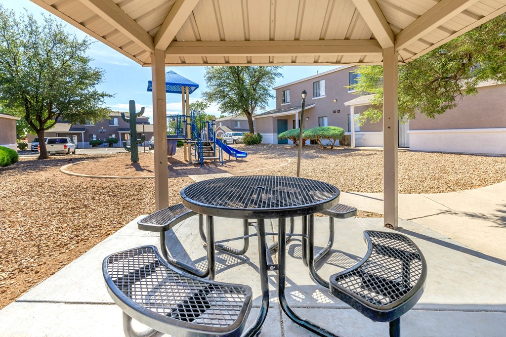 A playground with a table and chairs under a canopy.