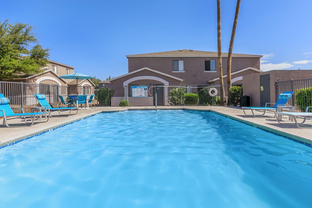 A swimming pool in front of a house with a fence and palm tree.