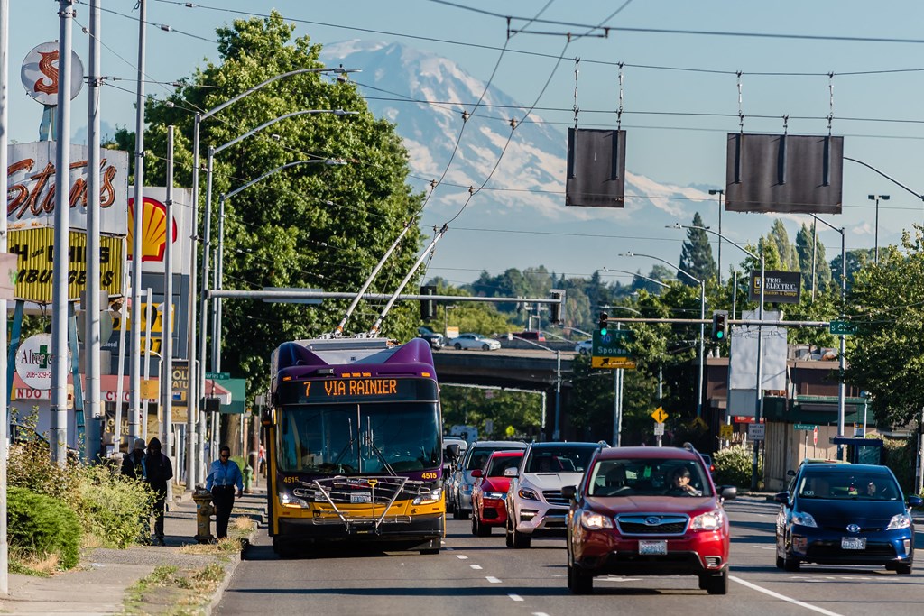 Bus at bus stop with Mount Rainier in the background and cars driving down the street.