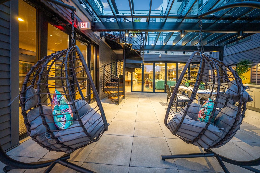 Two hanging chairs with cushions and a surfboard design are in front of a building with a glass ceiling.