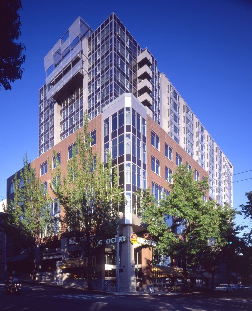 A tall building with a glass facade stands next to a tree.