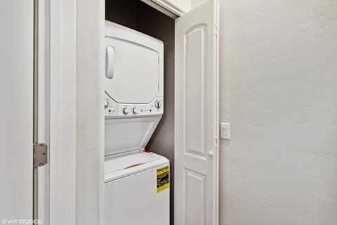 A white fridge is in a narrow space between a door and a wall.