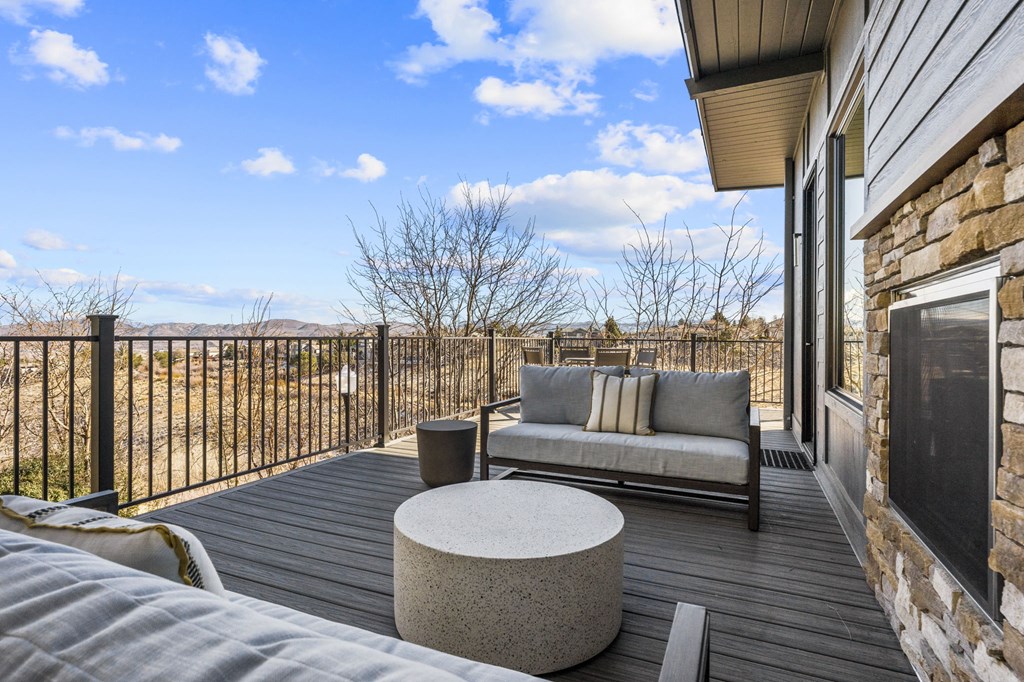 A wooden deck with a grey couch and a round table.