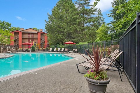 A pool area with a red umbrella and a black fence.