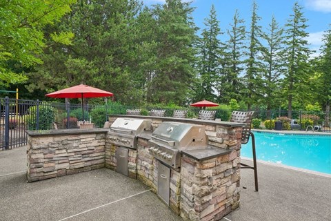 A backyard with a pool and a stone barbecue.