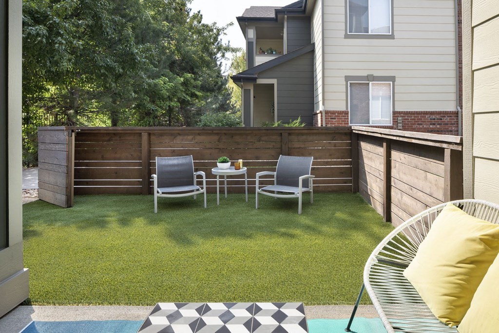 a backyard with a wooden fence and a patio with two chairs and a table