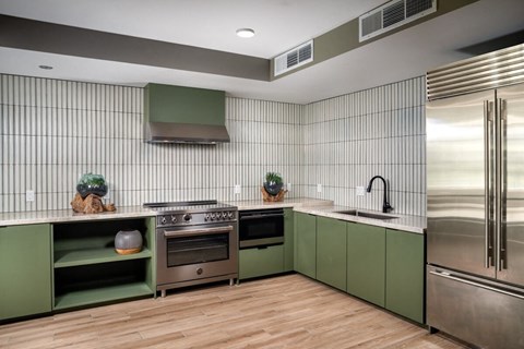 A modern kitchen with green cabinets and stainless steel appliances.