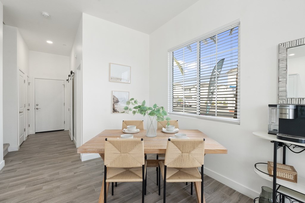 A dining room with a table set for two and a potted plant on the windowsill.