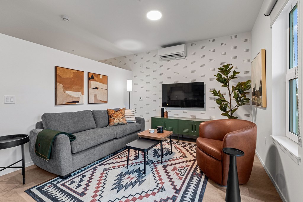 A living room with a grey couch, a brown leather chair, a coffee table, and a rug.