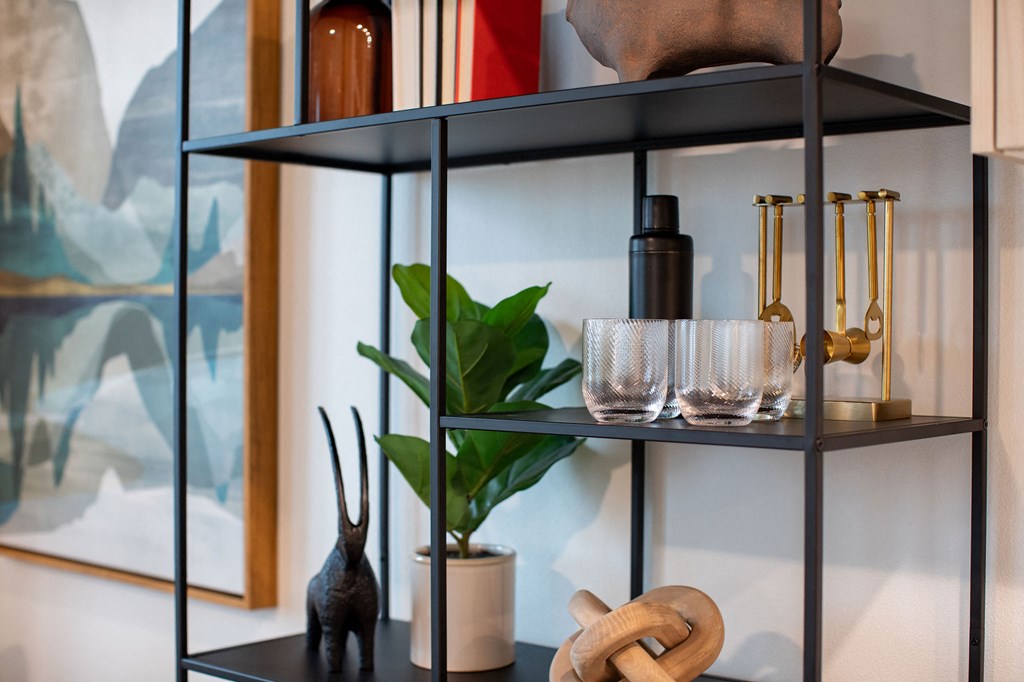 A black shelf with a variety of objects including a plant, glasses, and a bottle.