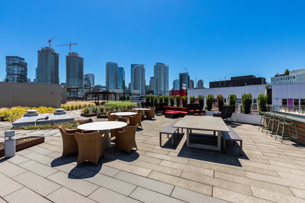 A rooftop patio with tables and chairs overlooking a city skyline.