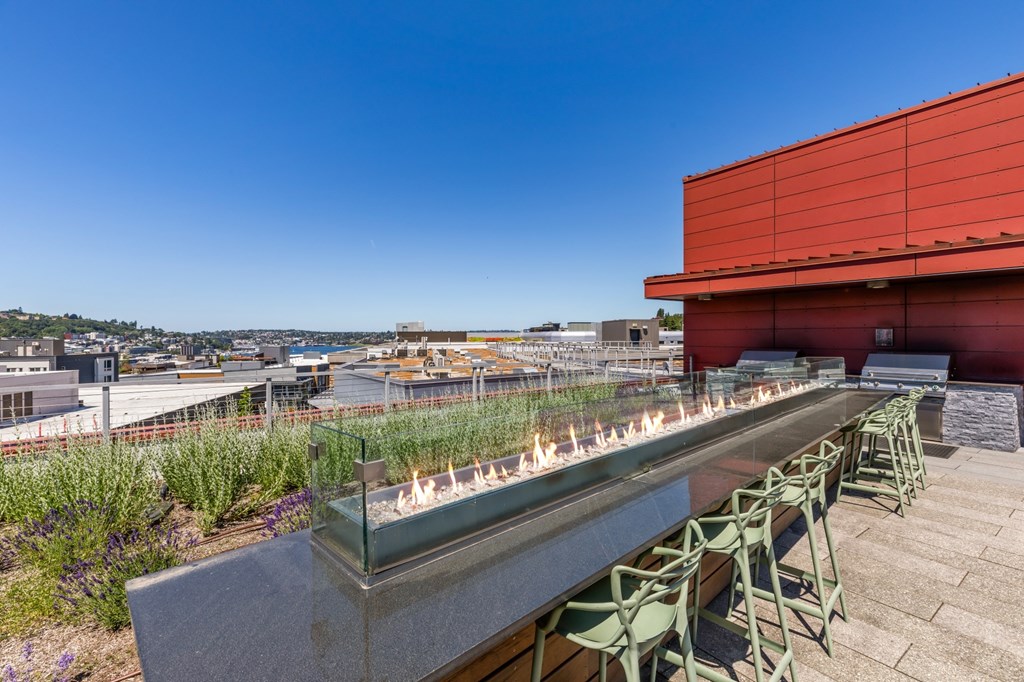 A rooftop patio with a long table and chairs overlooking a cityscape.