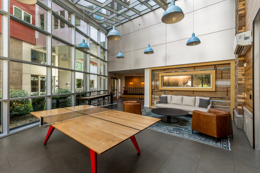 A large wooden table with red legs is in the middle of a room with a glass ceiling.