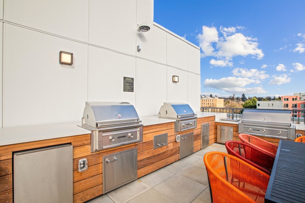 the cookout area of a rooftop patio with barbecue grills and chairs