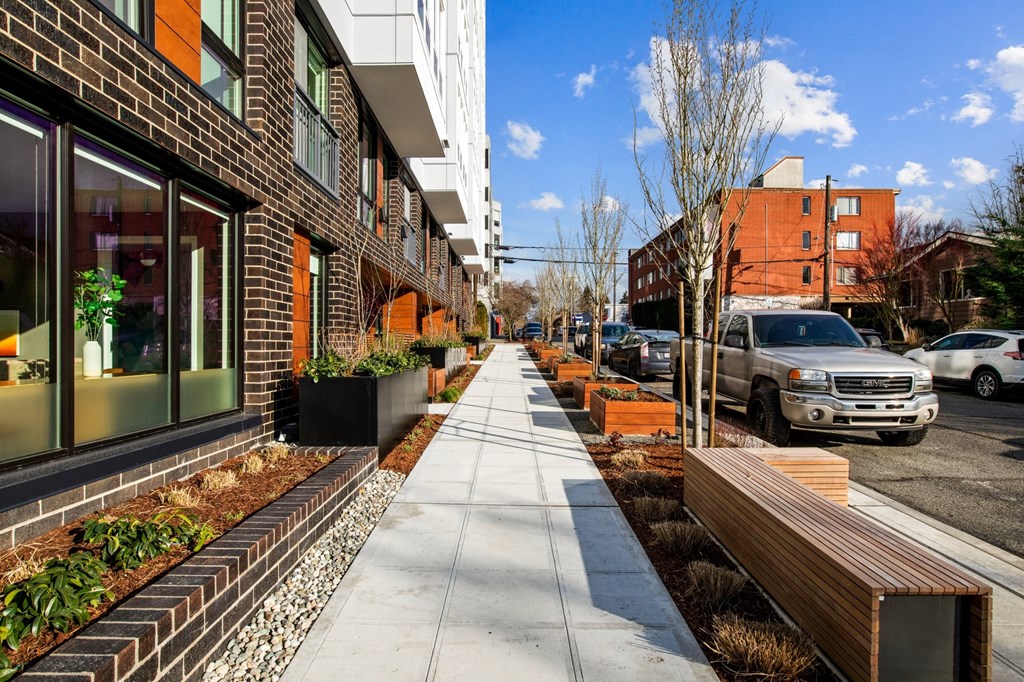 a sidewalk in front of a building with benches and plants