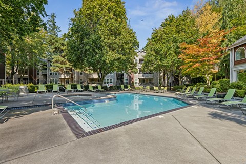 A swimming pool surrounded by trees and lounge chairs.