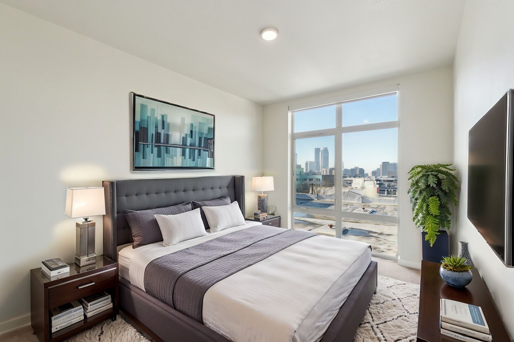 A bedroom with a large bed and a city view through the window.
