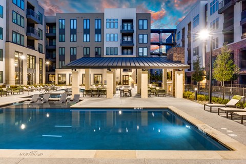 A large swimming pool in front of a building with a sun lounger and a table.