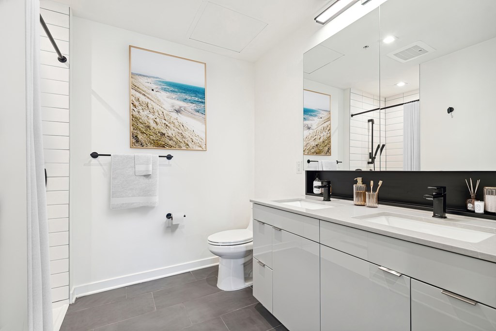 A modern bathroom with a toilet, sink, and a picture of a beach on the wall.