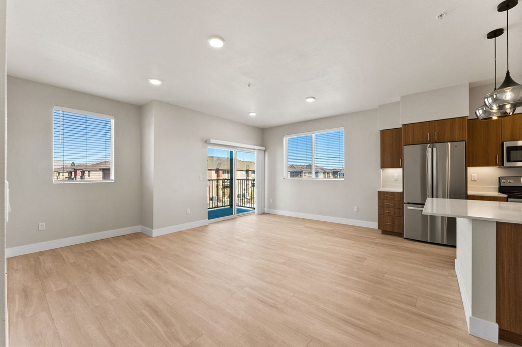 an empty living room with a kitchen and a stainless steel refrigerator