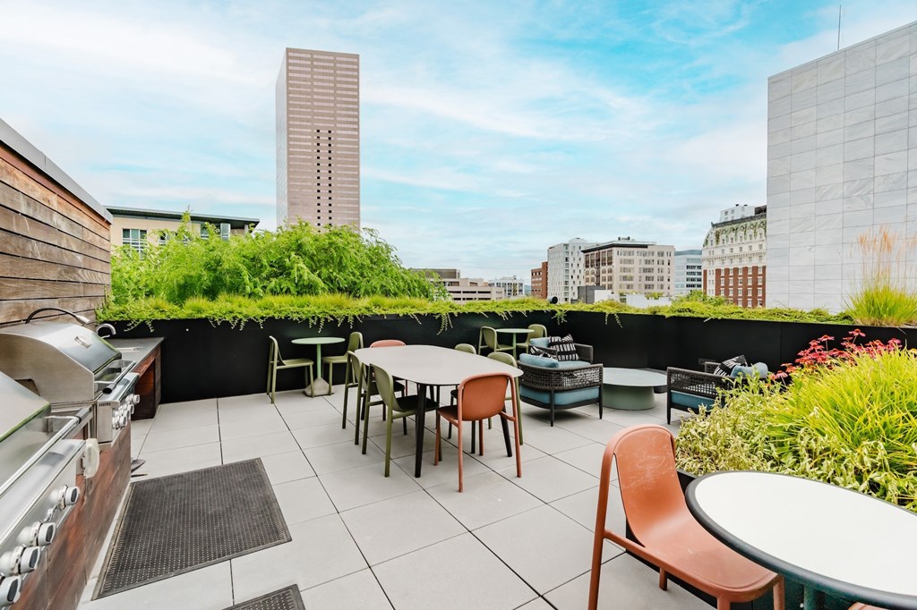 A rooftop patio with tables and chairs overlooking a city skyline.
