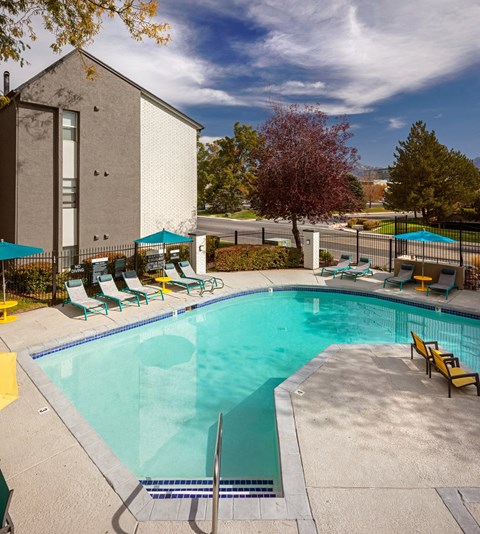 Swimming pool with lounge chairs and surrounding fence at Clover Creek Apartments, Murray, UT 84123