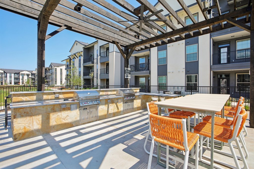 A patio with orange chairs and tables is covered by a wooden roof.