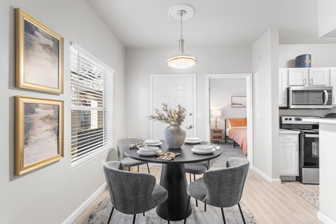 A dining room with a table set for four and a kitchen in the background.