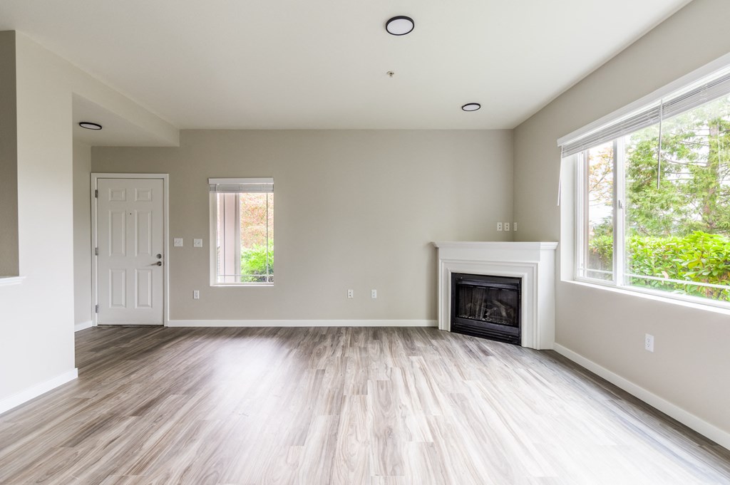 an empty living room with a fireplace and two windows