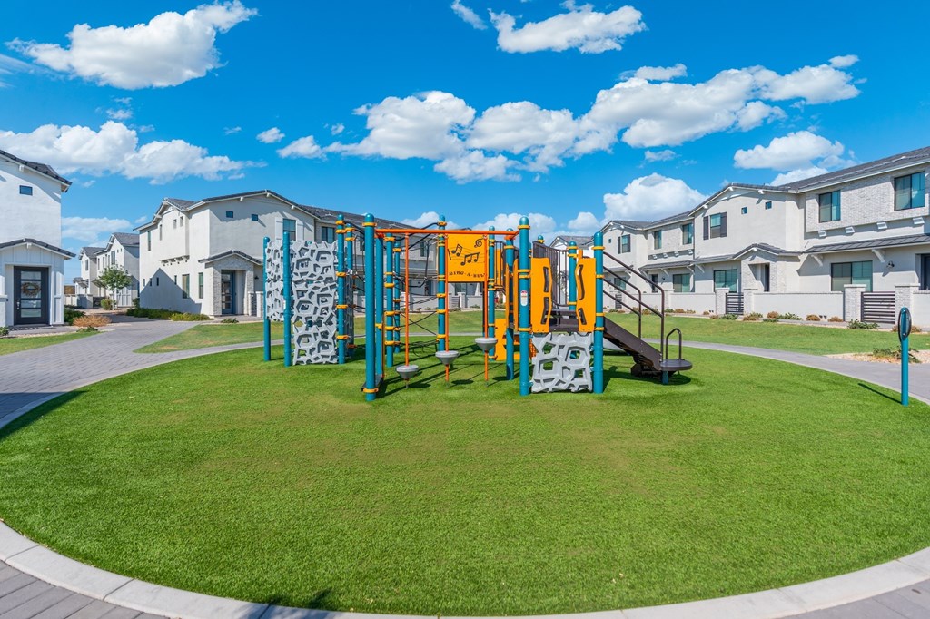 A playground with a slide and climbing wall in the middle of a grassy area.