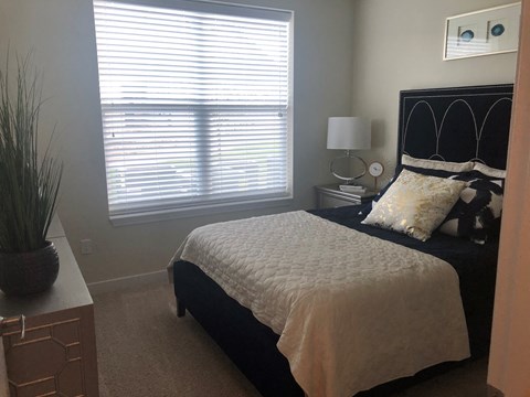 A bedroom with a bed, nightstand, and window with blinds.