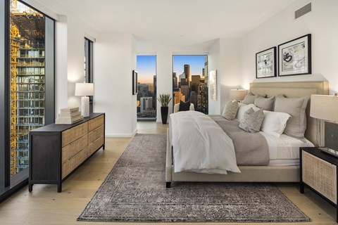 A bedroom with a large bed and a city view through the window.