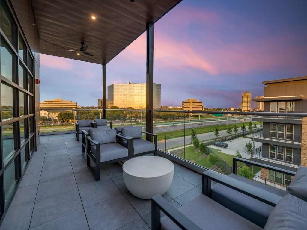 A balcony with a table and chairs overlooking a cityscape at dusk.