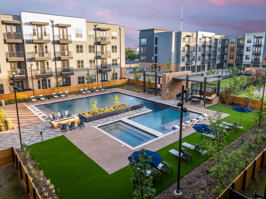 A swimming pool surrounded by a grassy area and apartment buildings.