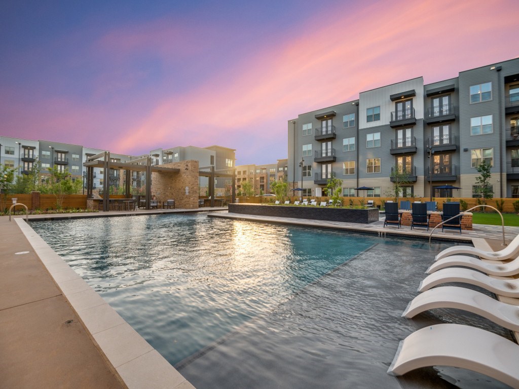 A swimming pool in front of apartment buildings at dusk.