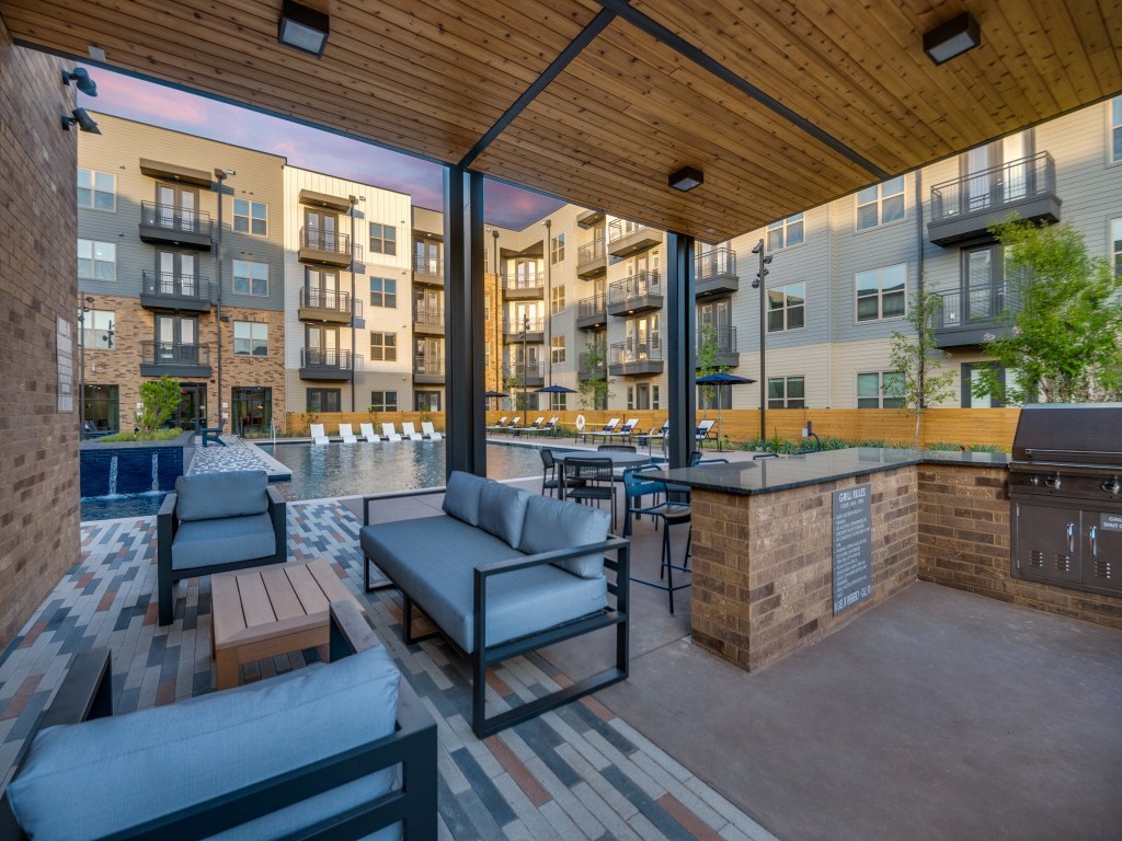 A patio with a couch, chairs, and a barbecue grill.