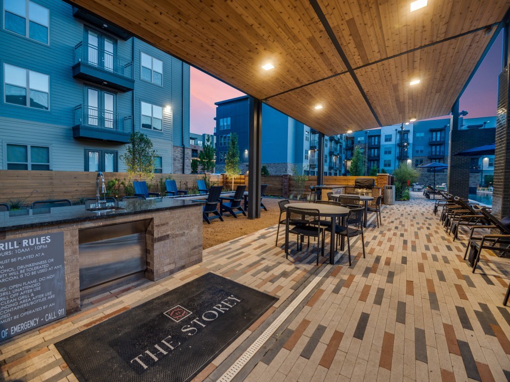 A patio area with tables and chairs under a wooden roof.