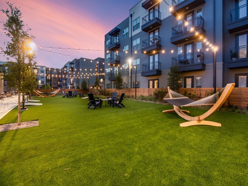 A hammock is set up in a grassy area in front of apartment buildings.