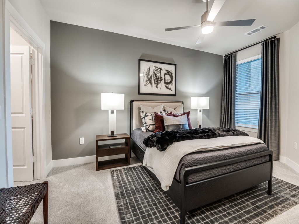 A bedroom with a large bed, a ceiling fan, and a painting on the wall.
