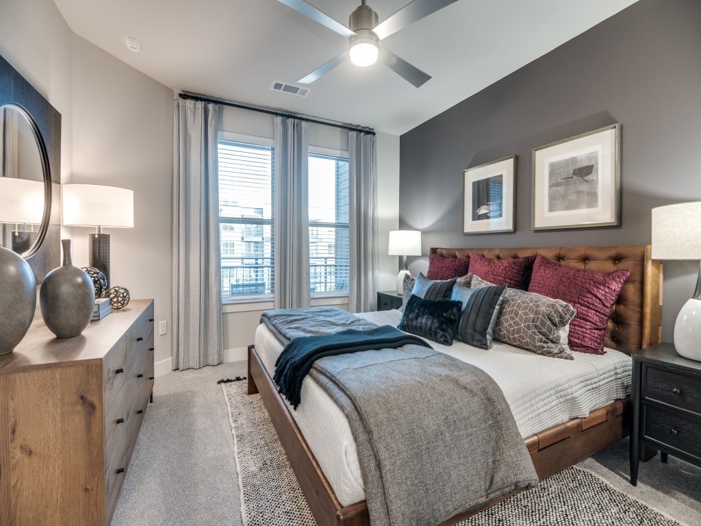 A bedroom with a large bed, a wooden dresser, and a ceiling fan.