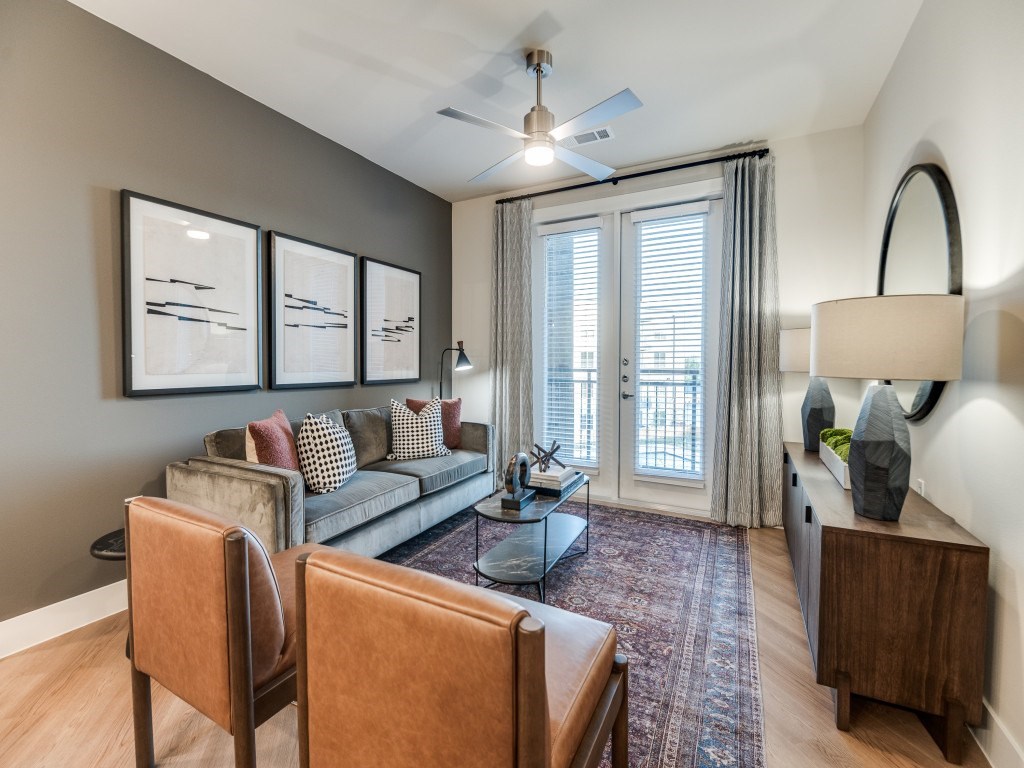 A living room with a grey couch, a brown chair, a coffee table, and a ceiling fan.